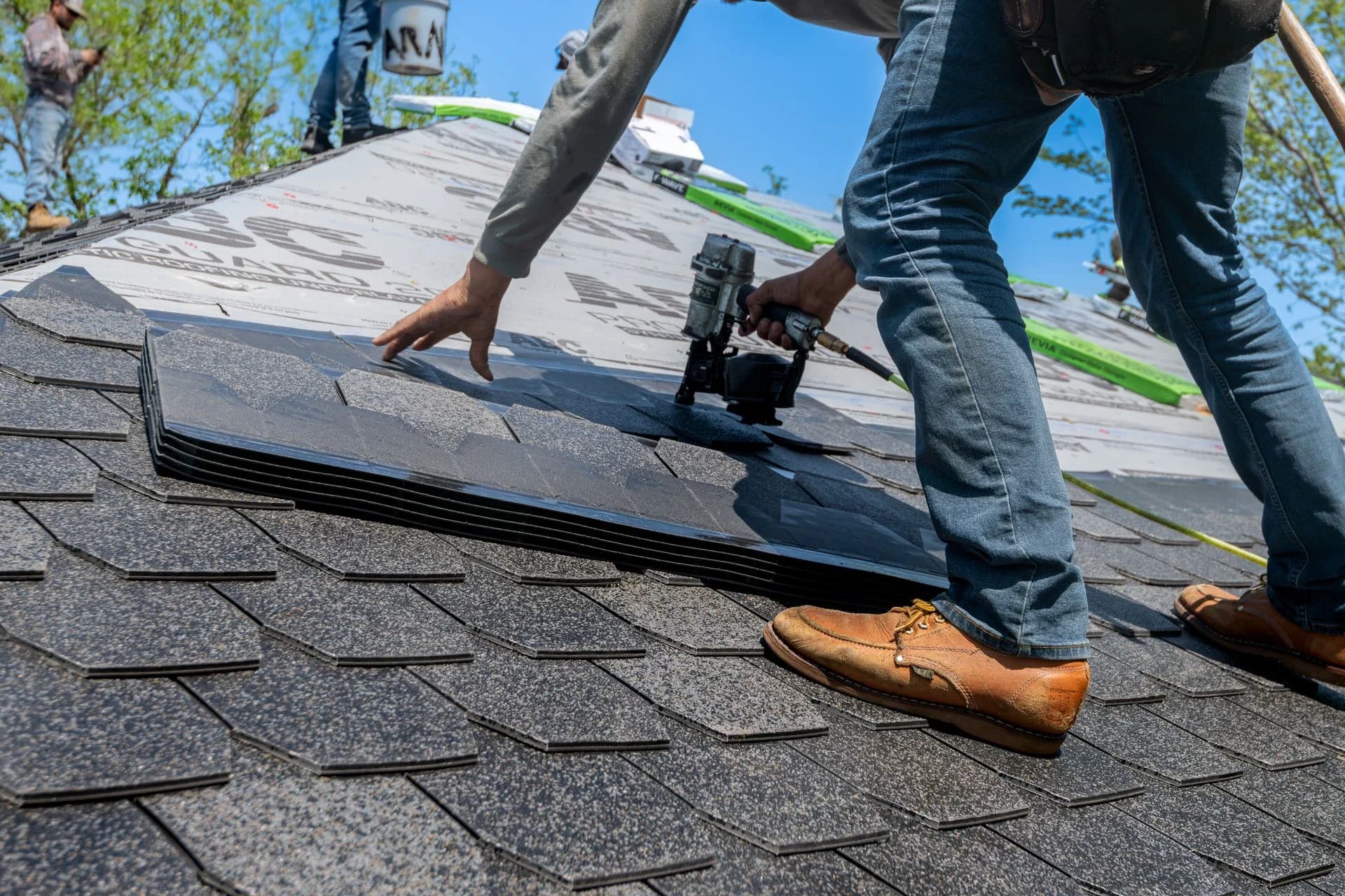 Roofer nailing asphalt shingles over underlayment on a new roof